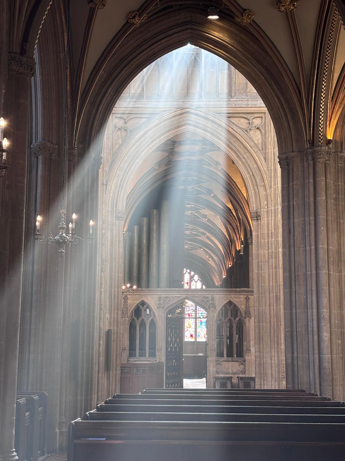 Long shafts of light pouring through the vaulted nave of a cathedral, stone pews below